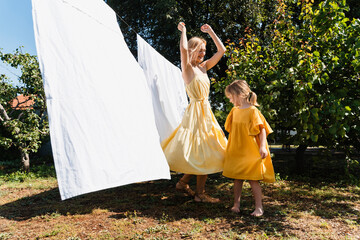 Mother and daughter dancing by white bedsheet hanging on clothesline at back yard