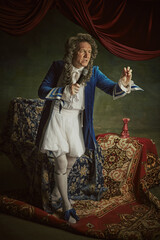 Elderly man dressed historical baroque-style attire, looks as king, singing to megaphone against...