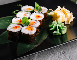 Sushi array garnished with wasabi and ginger on a stylish black plate, adorned with greenery