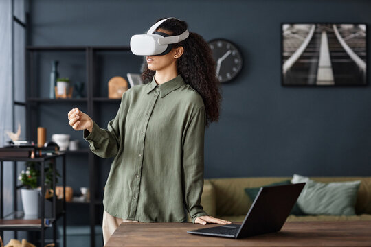 Young biracial woman wearing VR headset standing at table in living room at home surfing Internet, copy space