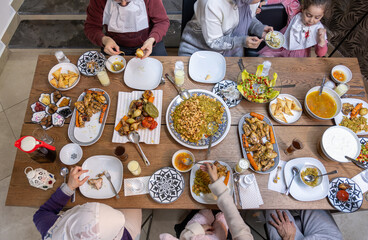 A Muslim family gathers around a rectangular table, sharing a heartwarming meal together, with members of various ages adding to the warmth and joy of the occasion