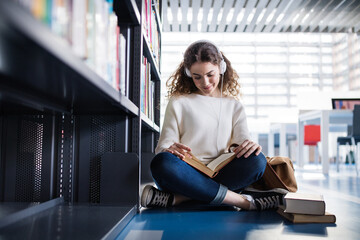 Young female student in library, focusing on final project, presentation. University student...