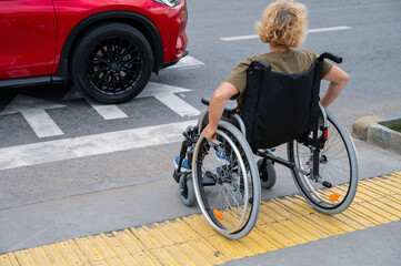 Fototapeta premium Rear view of an elderly Caucasian woman in a wheelchair crosses the road at a pedestrian crossing.
