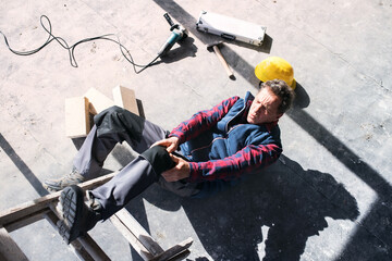 Male worker lying on the floor after fall from ladder, holding his knee. Work injury, accident in...
