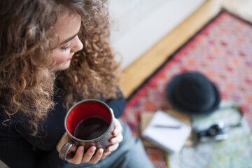 Beautiful woman planning summer vacation abroad, going on trip alone. Drinking coffee, looking at unpacked things.