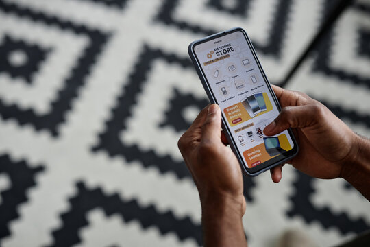 High angle view closeup of hands of unrecognizable Black man holding smartphone with online store app on screen, copy space