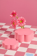 High angle shot at two pedestal in flower shaped displayed on pink checkered tablecloth with flor gerbera daisy decoration. Vertical photo for promotion with blank space for showing product