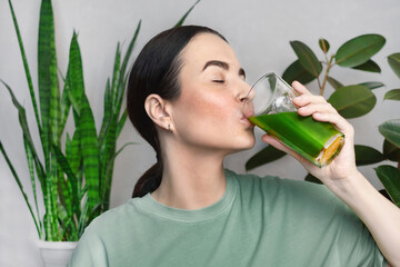 Woman drinking green healthy smoothie, drink. She drinks green wheatgrass energy shake.