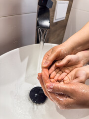 mother washes the child's hands with soap in the bathroom sink. The concept of cleanliness