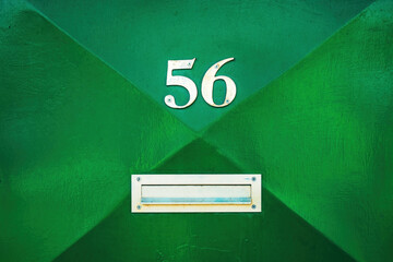 House number 56 on green metal door and mailbox slot. Fifty six in worn metallic numerals