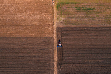 Tractor with tiller equipment plowing farmland soil, aerial shot