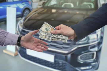 Businessman giving or paying money to dealer at modern car showroom