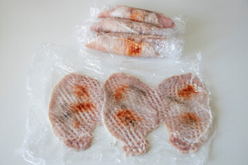 Preparing meat for chops. A raw pork chops, cut into pieces and sprinkled with spices covered with cling film.