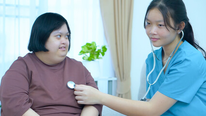 Asian female nurse uses stethoscope to perform physical examination of woman with Down syndrome at...
