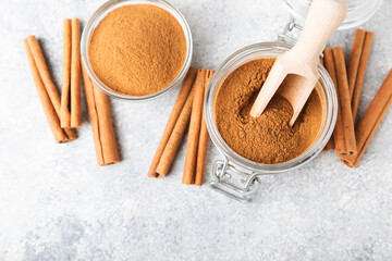 Cinnamon powder in a bowl on a textured wooden background. Spicy spice for baking, desserts and drinks. Fragrant ground cinnamon. Cinnamon stick. Place for text. Copy space.