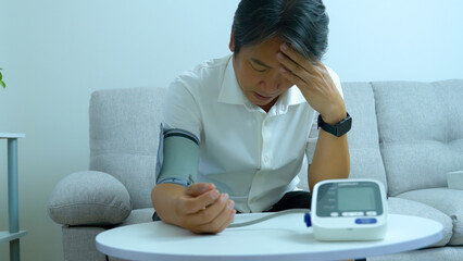 A middle aged asian man Unhappy with measuring blood pressure at home health care concept.