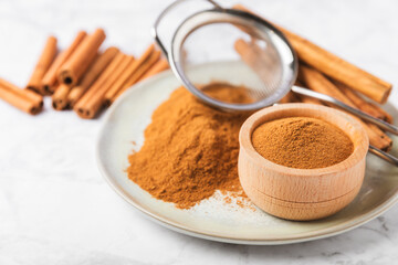 Cinnamon powder in a bowl on a textured wooden background. Spicy spice for baking, desserts and drinks. Fragrant ground cinnamon. Cinnamon stick. Place for text. Copy space.