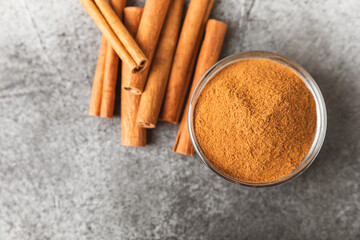 Cinnamon powder in a bowl on a textured wooden background. Spicy spice for baking, desserts and drinks. Fragrant ground cinnamon. Cinnamon stick. Place for text. Copy space.