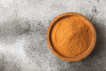 Cinnamon powder in a bowl on a textured wooden background. Spicy spice for baking, desserts and drinks. Fragrant ground cinnamon. Cinnamon stick. Place for text. Copy space.