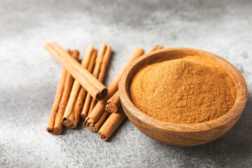 Cinnamon powder in a bowl on a textured wooden background. Spicy spice for baking, desserts and drinks. Fragrant ground cinnamon. Cinnamon stick. Place for text. Copy space.