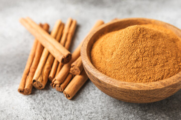 Cinnamon powder in a bowl on a textured wooden background. Spicy spice for baking, desserts and drinks. Fragrant ground cinnamon. Cinnamon stick. Place for text. Copy space.