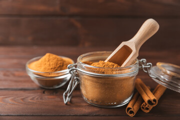 Cinnamon powder in a bowl on a textured wooden background. Spicy spice for baking, desserts and drinks. Fragrant ground cinnamon. Cinnamon stick. Place for text. Copy space.