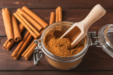 Cinnamon powder in a bowl on a textured wooden background. Spicy spice for baking, desserts and drinks. Fragrant ground cinnamon. Cinnamon stick. Place for text. Copy space.