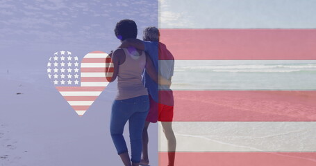 Fototapeta premium Image of america flag in heart over american flag, african american couple walking on beach
