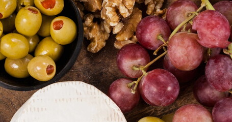 Image of wooden bowl of cheese, grapes, nuts and olives over green vegetables