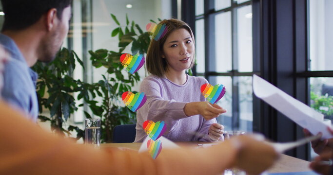 Multiple rainbow heart icons floating over group of diverse office colleagues discussing at office - Powered by Adobe