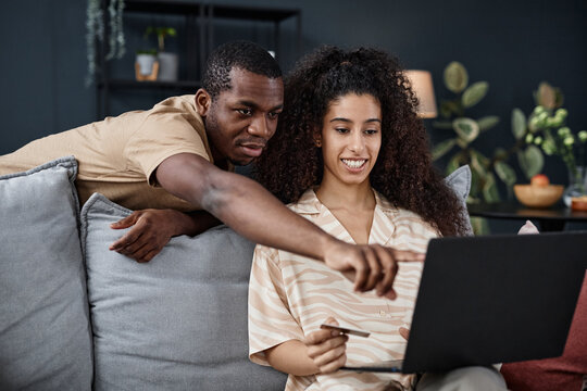 Medium shot of young Black man and biracial woman spending time together at home doing online shopping on laptop