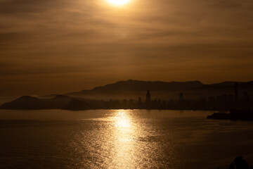 Photo of the sun setting over the ocean and the town of Benidorm in Spain