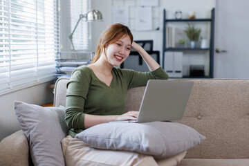 Asian business woman working on a laptop on couch, tax, accounting, statistics and analytical research concept.