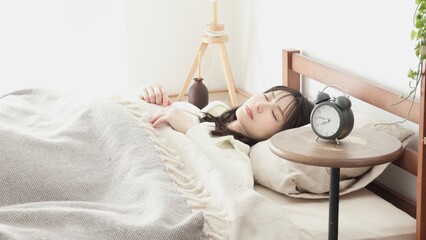 目覚まし時計をセットして寝る女性