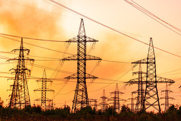 A large number of power lines are visible in the sky, with some of them being very tall. The sky is orange and the sun is setting - Powered by Adobe