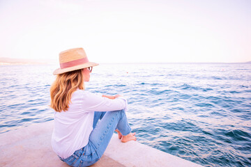 Rear view of a middle-aged woman sitting on the pier and enjoying the view of the sea