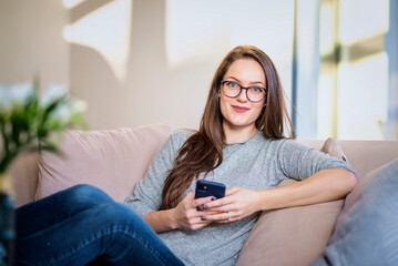 Smiling brunette haired woman using smartphone and relaxing at home