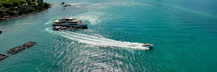 Luxury yacht cruising near tropical coastline with speedboat in tow, ideal for summer vacation and...