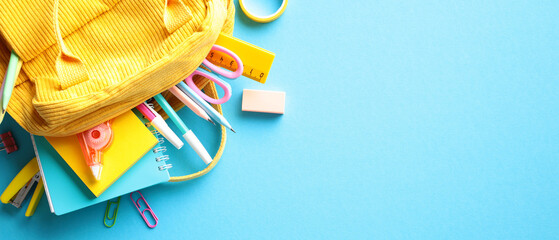 Vibrant school essentials spilling from a yellow backpack on a blue backdrop, perfect for...