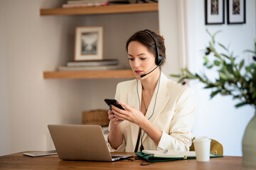 Customer service assistant businessswoman wearing headset and using smartphone and workign from home