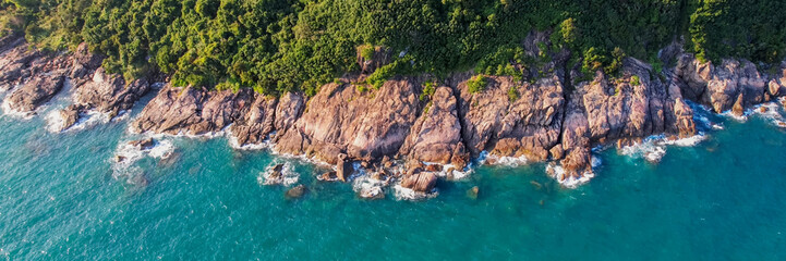 Aerial view of a rugged coastline with lush greenery meeting turquoise waters, ideal for travel and...
