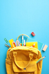 Yellow corduroy backpack overflowing with colorful school supplies, set against a striking blue...