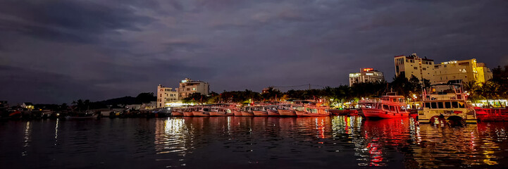 Twilight harbor scene with illuminated fishing boats and waterfront buildings reflecting on calm...