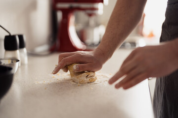 A person kneading dough with flour on a kitchen counter, focused on hands.