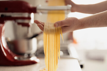 A close-up of hands cutting fresh pasta dough using a kitchen appliance.