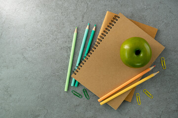 Notebook and colored pencils and green apple on stone texture background. Work desk space