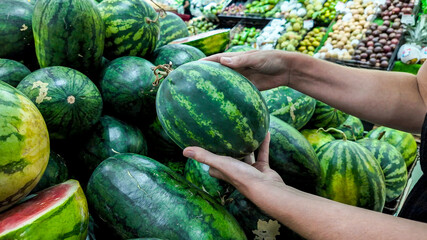 Person selecting fresh watermelons at a local farmers market, depicting healthy eating and summer...