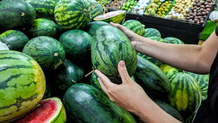 Person selecting fresh watermelons at a local farmers market, depicting healthy eating and summer harvest, ideal for National Watermelon Day promotions