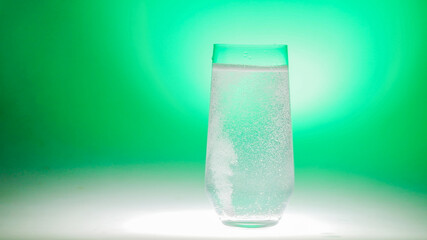 Effervescent water in a clear glass against a vibrant green backdrop, suggesting themes of refreshment, St Patrick's Day celebrations, or healthy lifestyle concepts