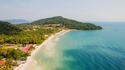 Aerial view of a tranquil tropical beach with lush greenery on a sunny day, ideal for travel and summer vacation concepts